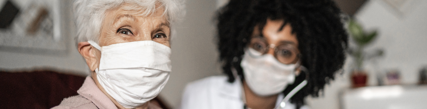 Older woman in mask sitting with young doctor in mask