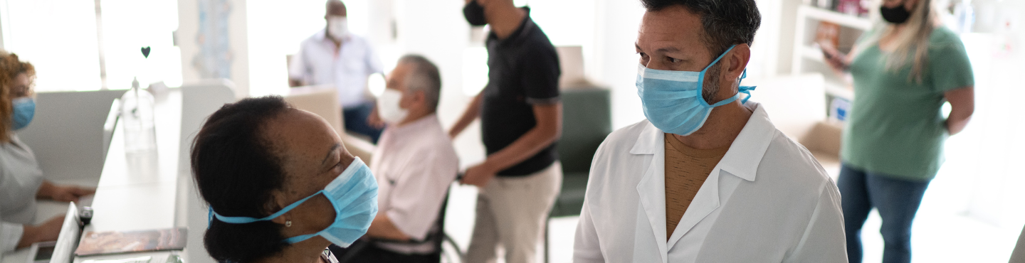 two doctors with mask have a discussion with patients in the background